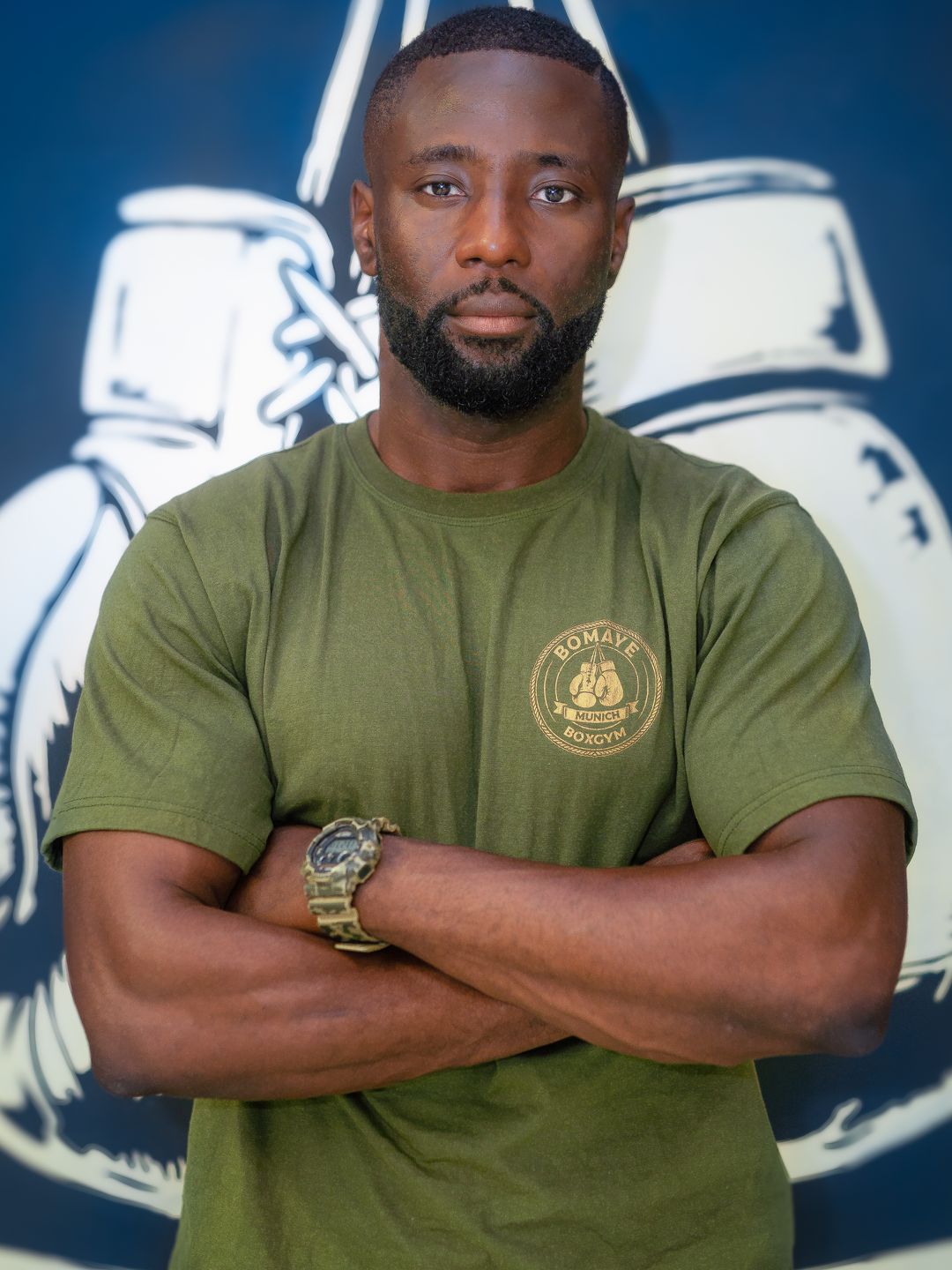 Coach des Bomaye Gym München im Portrait vor der Bomaye-Wand